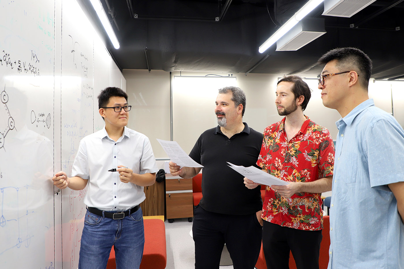Four scientists stand talking at a whiteboard.